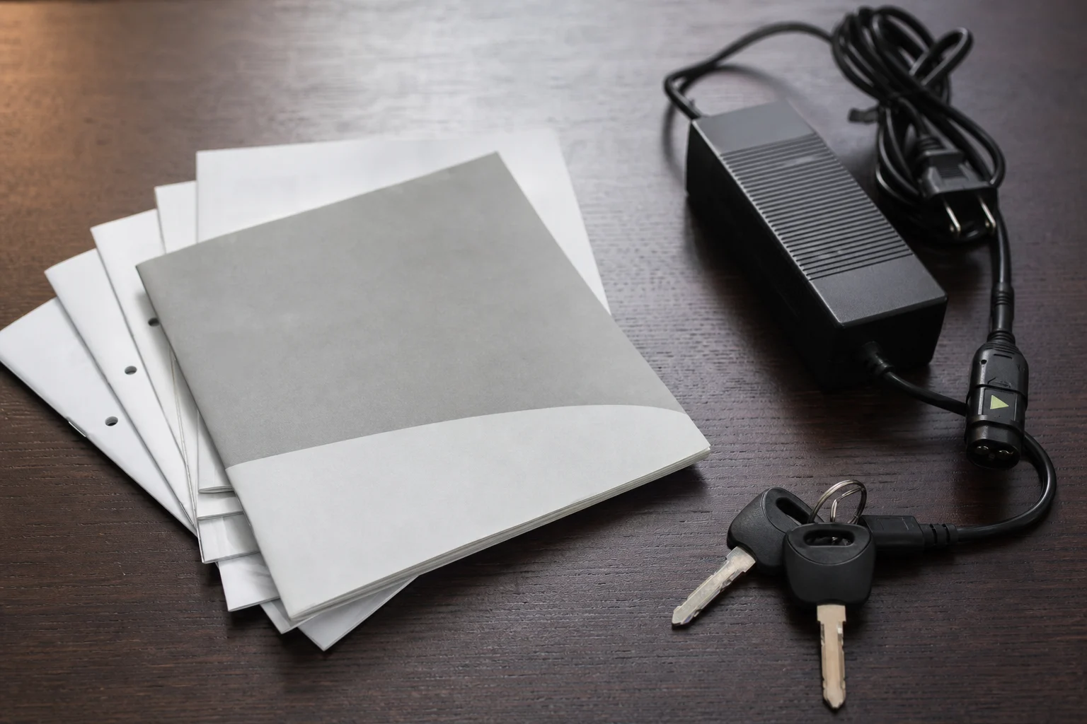 Documentación, llave, cargador y cable de una moto eléctrica usada sobre una mesa